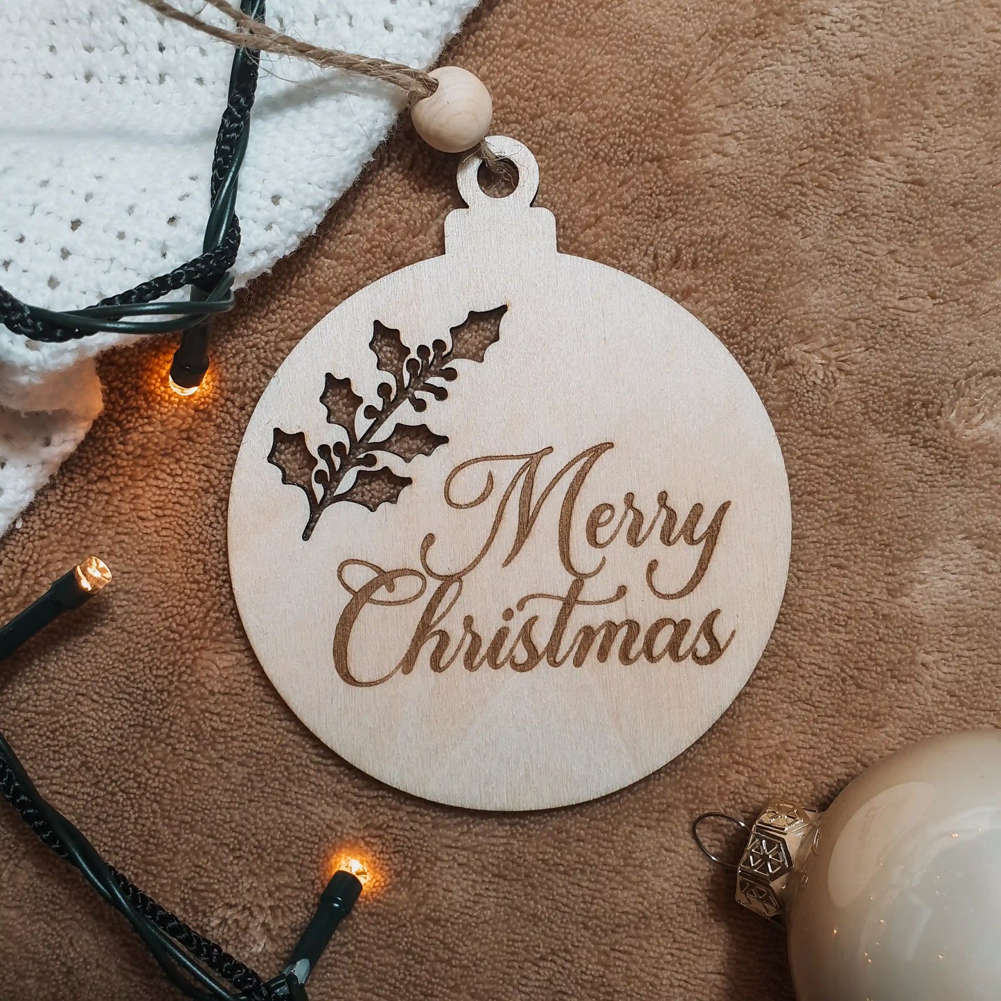 Houten kerstbal met uitgesneden kersttak en gegraveerd met de tekst "Merry Christmas".