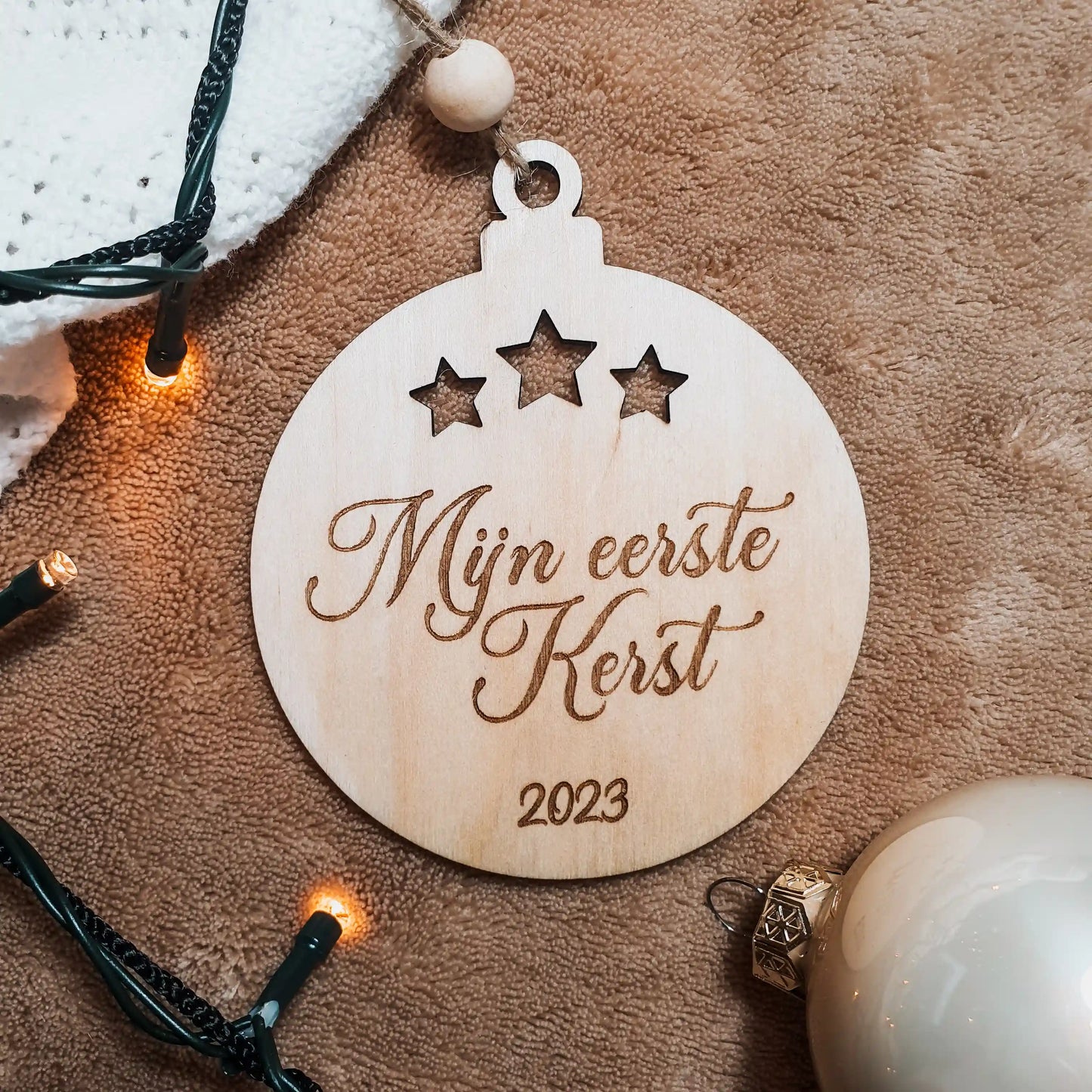 Houten kerstbal met uitgesneden sterretjes, gegraveerd met de tekst "Mijn eerste Kerst" en het geboortejaar.