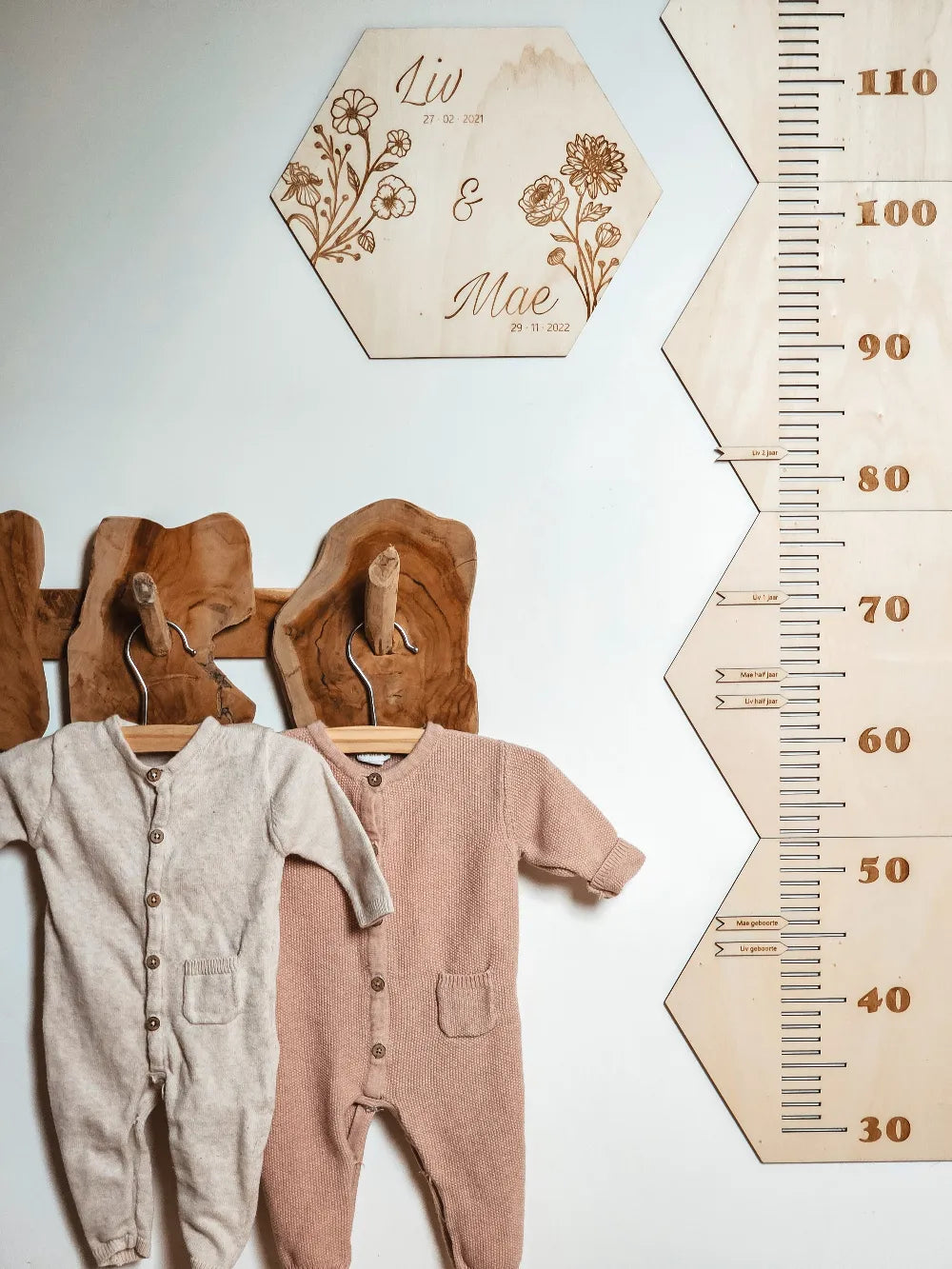 Houten groeimeter met naam in hexagon-vorm met geboortebloemen aan de muur van een kinderkamer.