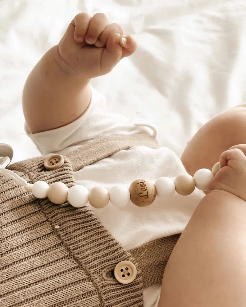 Baby met een speenkoord, gegraveerd met naam in witte en beige tinten.