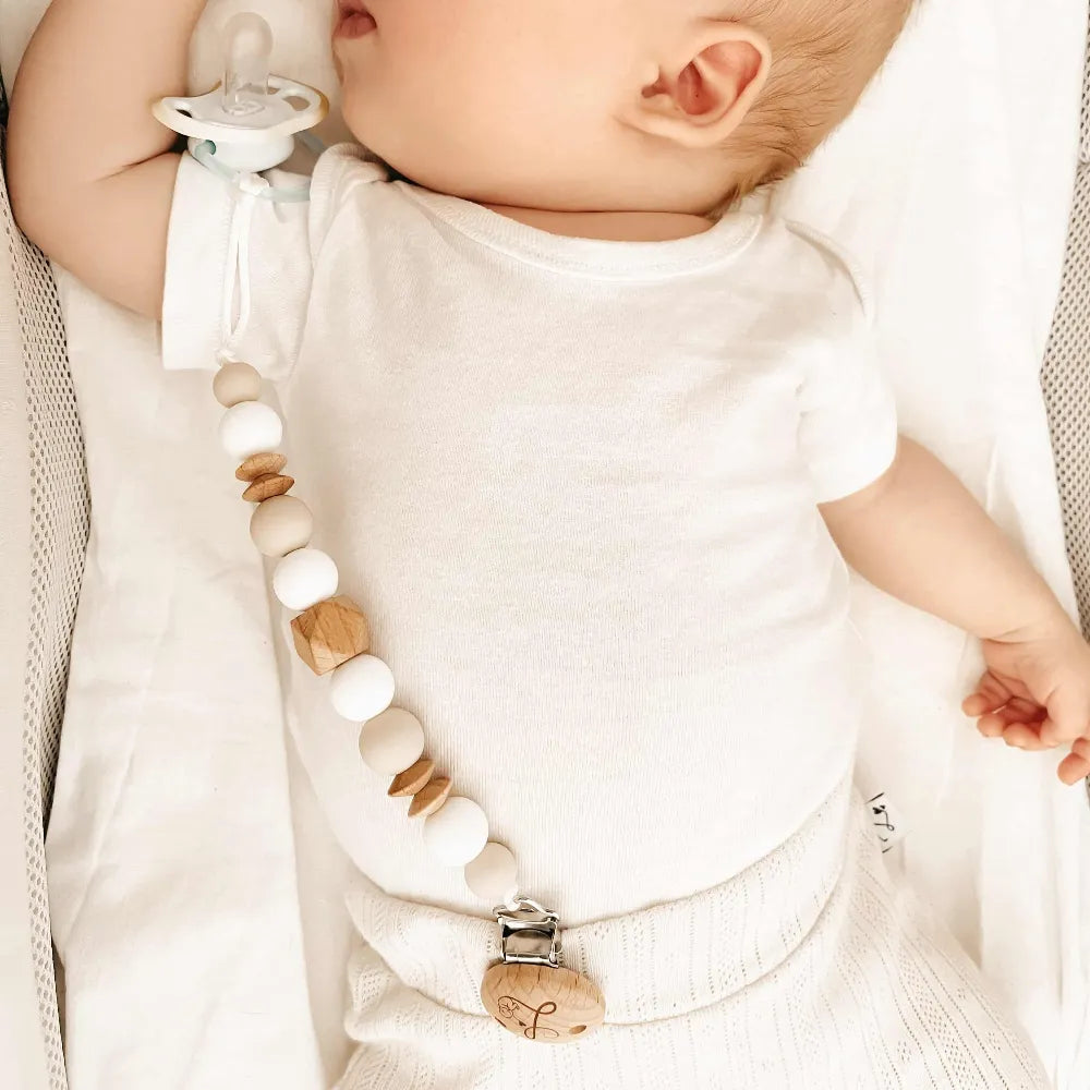 Slapende baby met een speenkoord van siliconen en houten kralen in zachte, neutrale tinten.