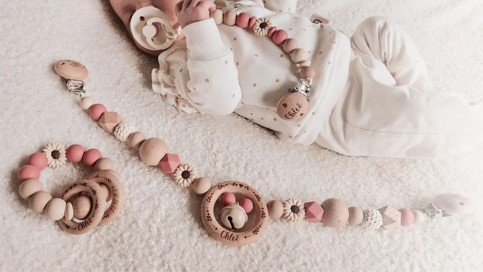 Baby met een gepersonaliseerde roze bijtring, wagenspanner en speenkoord, gegraveerd met naam.